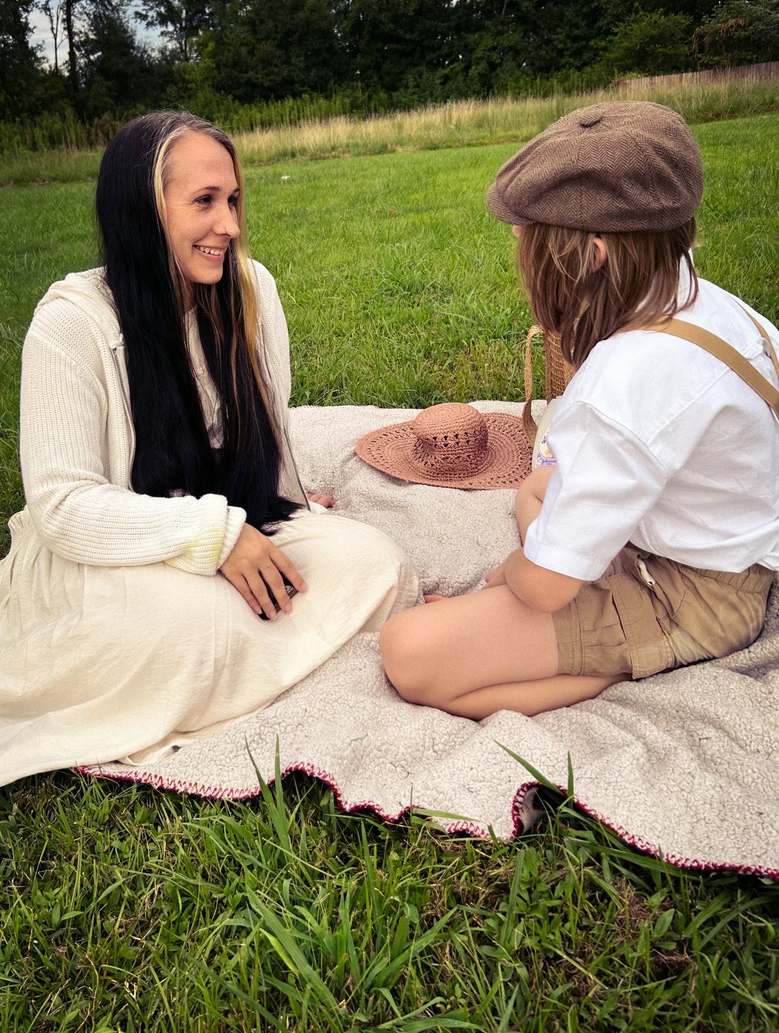 Lindsey sitting on a picnic blanket in a sunlit field, sharing a moment with her child